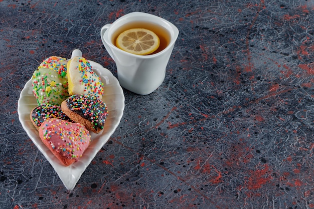 Um prato de biscoitos em forma de coração com granulado e uma xícara de chá quente