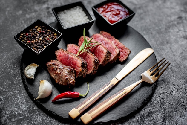 Um prato de carne com um garfo e duas pequenas tigelas de molhos e uma pimenta vermelha.