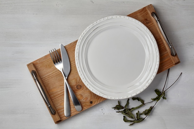 Um prato de cerâmica branca e uma bandeja de talheres sobre uma mesa de madeira pintada com luz