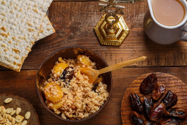 Um prato de cuscuz com açafrão e nozes em uma mesa de madeira ao lado de matzah e um jarro de caldo de frutas