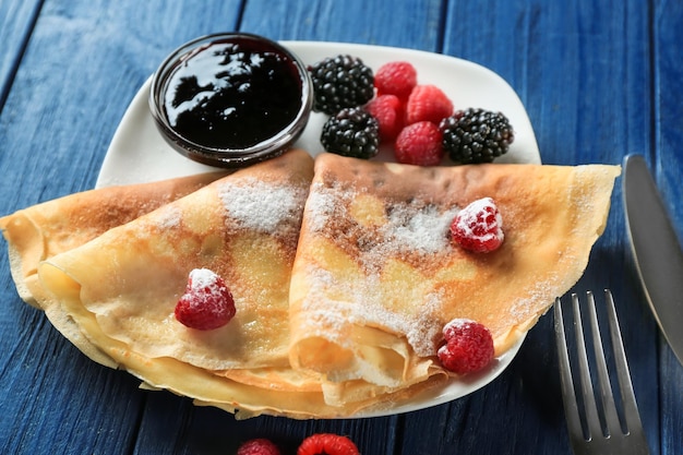 Foto um prato de deliciosas panquecas finas com bagas e geleia na mesa.