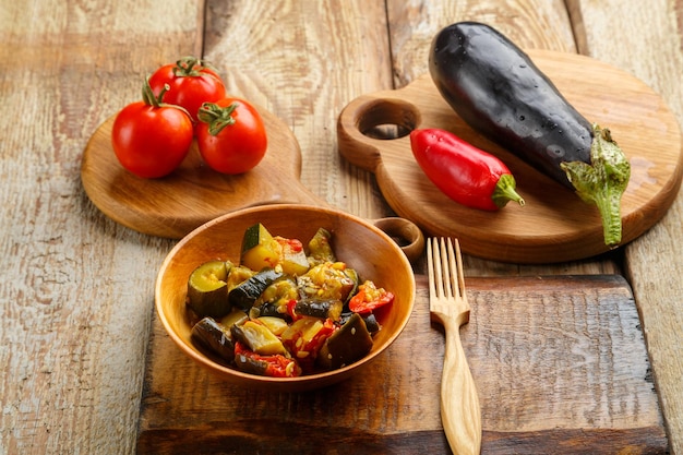 Um prato de legumes grelhados ao lado de tomate e berinjela em tábuas de madeira