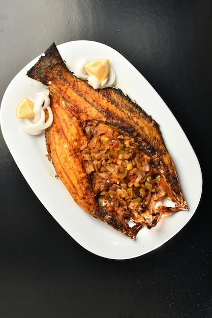 Um prato de peixe com cebola frita e uma rodela de limão.