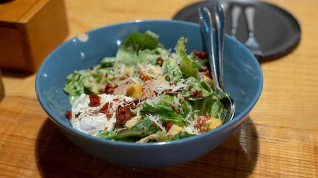 Um prato de salada caesar em um prato azul, apresentado em uma mesa de madeira.