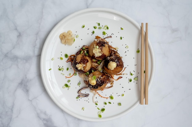 Um prato de takoyaki com pauzinhos sobre uma mesa de mármore