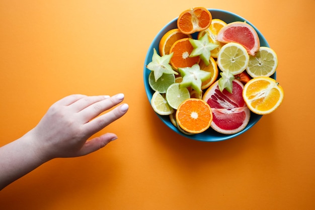 Um prato grande com frutas cítricas fatiadas e uma mão estendida para o prato