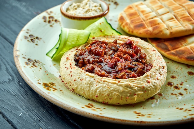 Um prato oriental clássico - hummus de grão de bico com vegetais assados e azeite de oliva servido com pita assada em uma mesa de prato de madeira