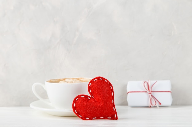 Um presente, coração vermelho, café da manhã contra o de uma parede de luz, conceito, um cartão postal para o dia dos namorados.