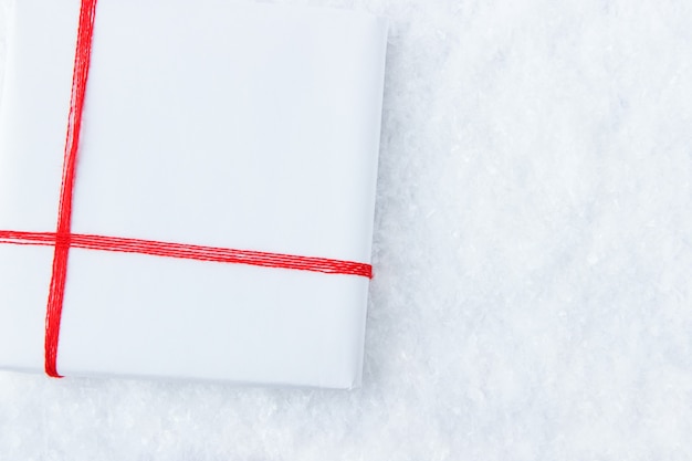 Um presente de cor branca amarrado com uma fita vermelha encontra-se na neve vista de cima no feriado de Natal
