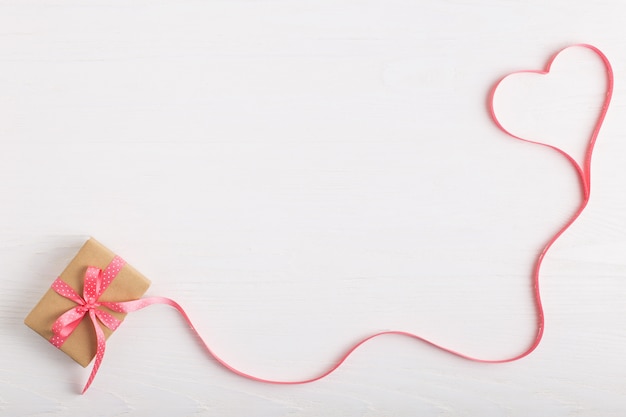 Um presente de papel ofício e uma fita rosa em uma mesa de madeira branca