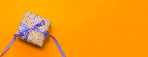 Um presente embrulhado em papel artesanal, amarrado com uma fita roxa em um fundo laranja