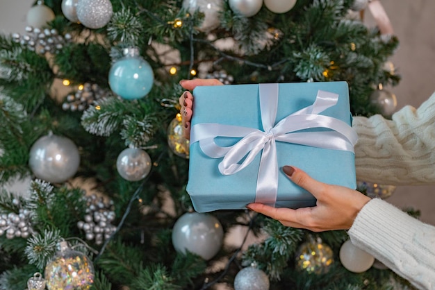 Um presente nas mãos da mulher contra o pano de fundo das luzes da árvore de Natal