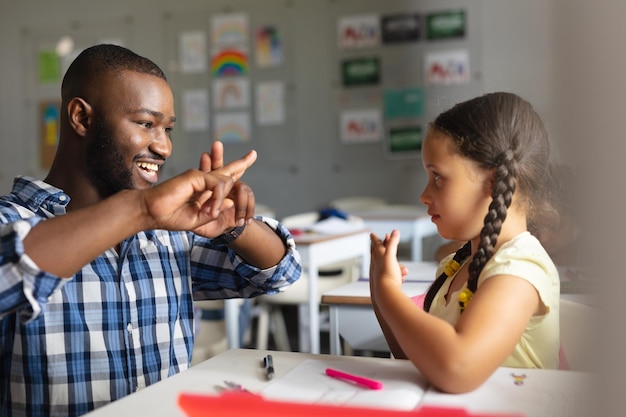 Um professor afro-americano sorridente a ensinar linguagem de sinais a uma rapariga caucasiana.