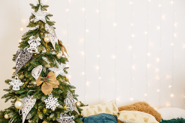Um quarto aconchegante decorado com guirlandas e árvores de Natal. A cama com almofada branca é elegante e moderna. Bom espírito de ano novo. Lugar de textura de fundo de cores claras para texto. Decoração do quarto para o feriado