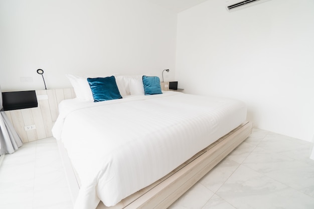 Um quarto branco com uma cama de madeira, roupa de cama e travesseiro com manto branco.