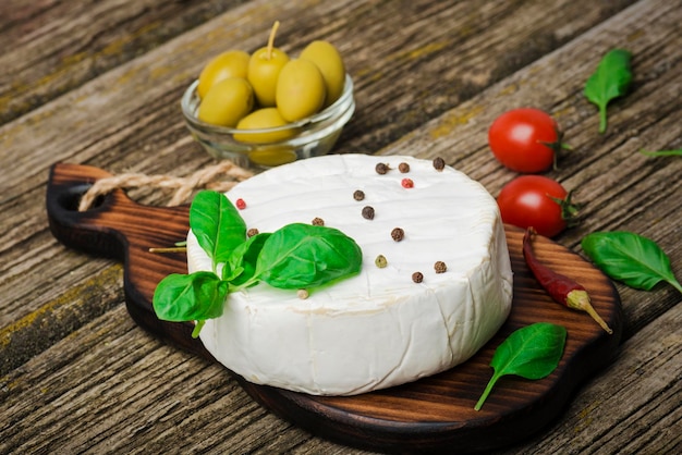 Um queijo com folhas de manjericão em uma placa de madeira