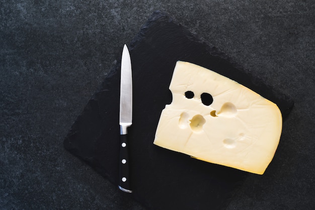 Foto um queijo sólido apetitoso em um prato preto com faca