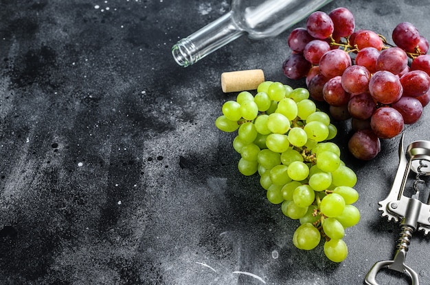 Um ramo de uvas verdes e vermelhas, uma garrafa, um saca-rolhas e uma rolha. conceito de vinificação. fundo preto