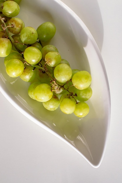 Um ramo de uvas verdes maduras em um prato branco sobre uma mesa branca