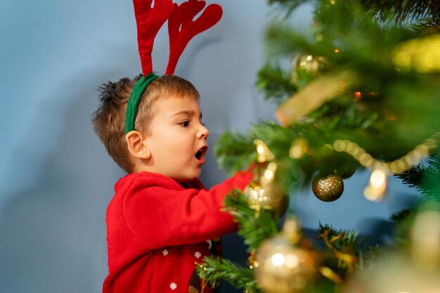 Um rapaz bonito a decorar uma árvore de natal em casa.