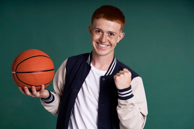 Um rapaz caucasiano de cabelo vermelho bem sucedido a segurar uma bola de basquetebol e a olhar para a câmara.