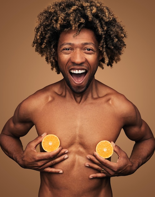 Foto um rapaz preto alegre sem camisa a cobrir o peito com laranjas e a rir.