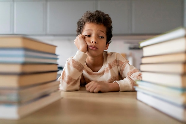 Foto um rapaz preto entediado a descansar a cabeça na mão e a olhar para pilhas de livros.