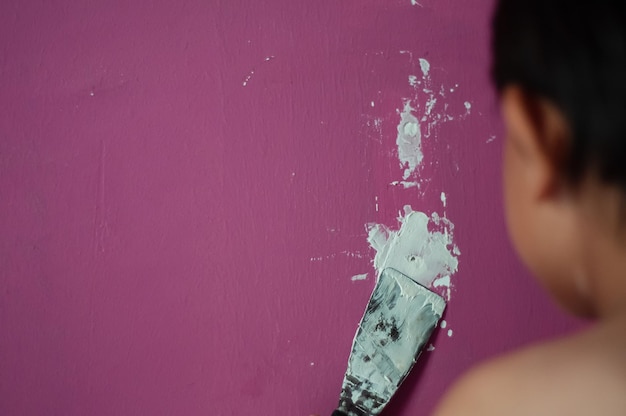 Foto um rapaz sem camisa a encher um buraco com uma faca na parede.