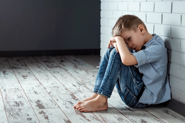 Um rapaz senta-se sozinho com um sentimento triste na escola perto da parede