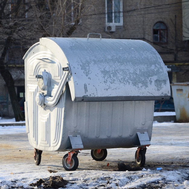 Um recipiente de lixo de prata fica perto de edifícios residenciais no inverno