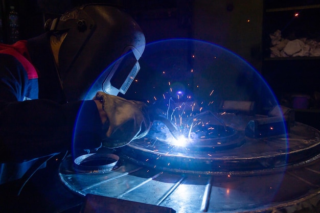 Um reflexo de lente durante a soldagem elétrica semiautomática manual com faíscas trabalhador industrial profissional em máscara protetora preta