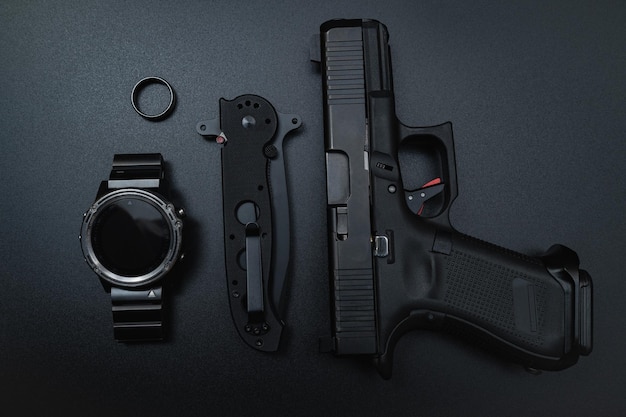 Um relógio, uma arma e um relógio estão dispostos sobre uma mesa preta.