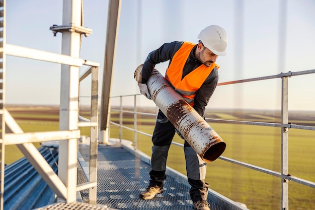 Um reparador carrega um tubo de metal pesado em grande altura