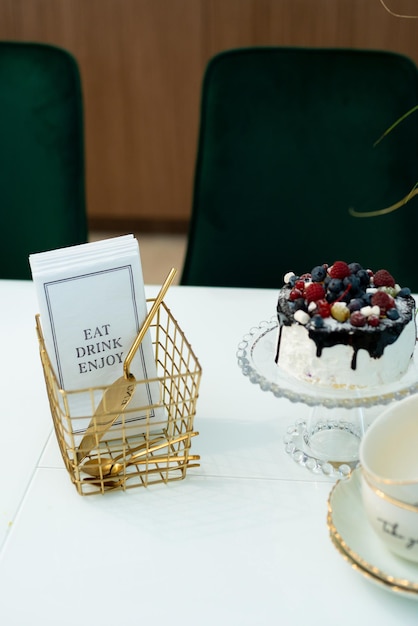 Um requintado bolo de frutas vermelhas em um suporte de vidro sobre uma mesa com um vaso de flores e um jogo de chá em um interior de design moderno. foco seletivo suave, ruído de arte