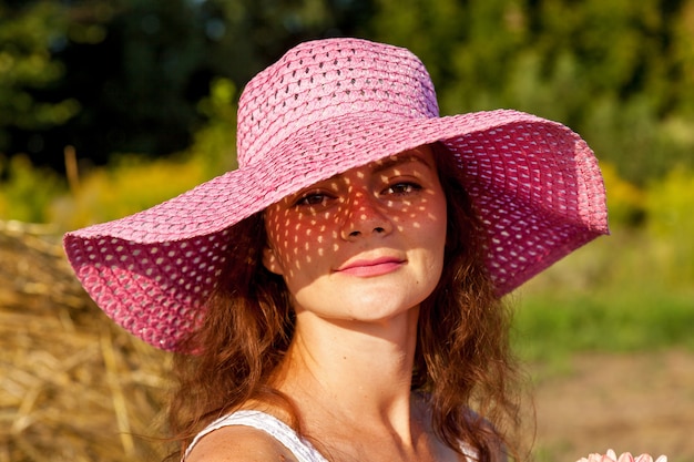 Um retrato ao ar livre de uma linda mulher de chapéu-de-rosa no fundo de um campo de trigo.