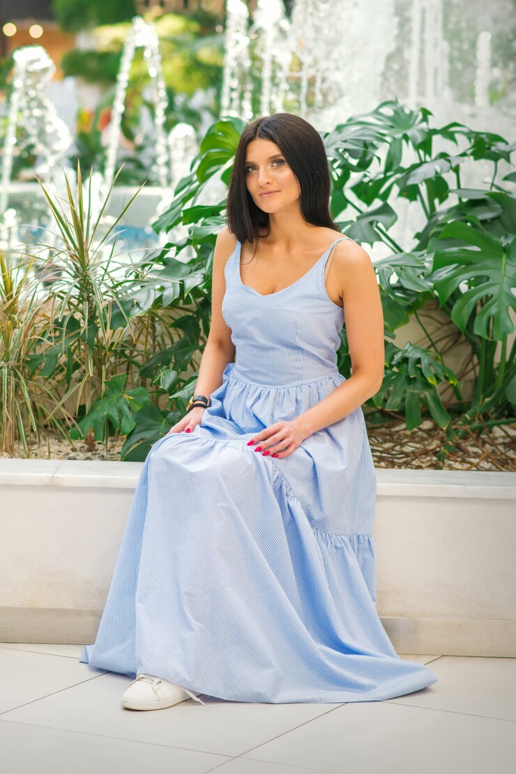 Foto um retrato ao ar livre de uma mulher morena atraente com um vestido longo azul está posando junto à fonte ...