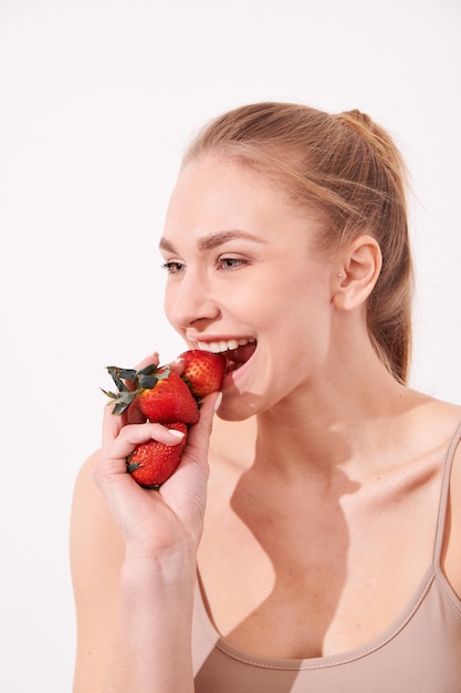 Foto um retrato criativo de uma linda garota segurando com uma mão um morango suculento perto de seus lábios com