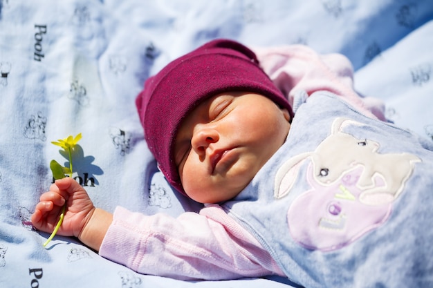 Um retrato da foto de um bebê com um boné vermelho encontra-se sobre uma manta branca na grama verde. A primavera está na rua, o sol está brilhando na criança