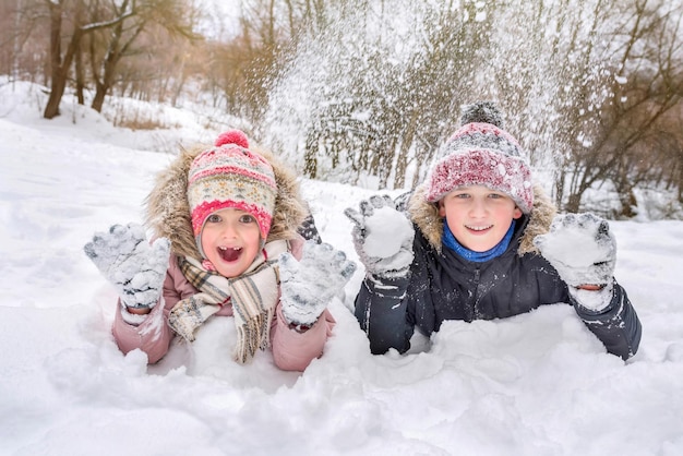 Um retrato de crianças de 5 e 10 anos deitadas na neve posando em uma câmera em um parque da cidade