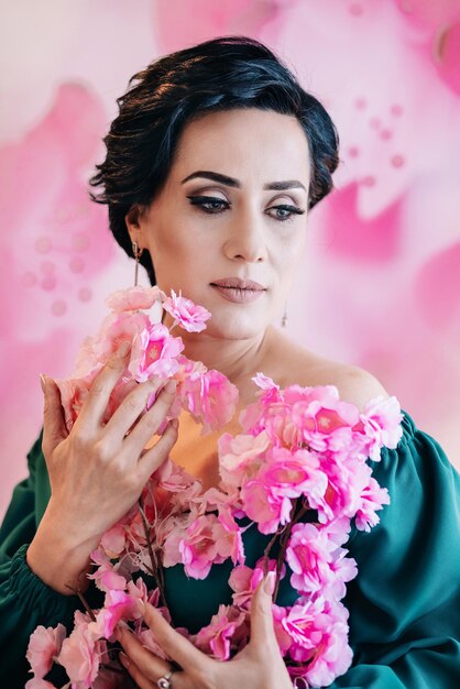 Foto um retrato de estilo de primavera de uma mulher bonita segurando flores cor-de-rosa artificiais