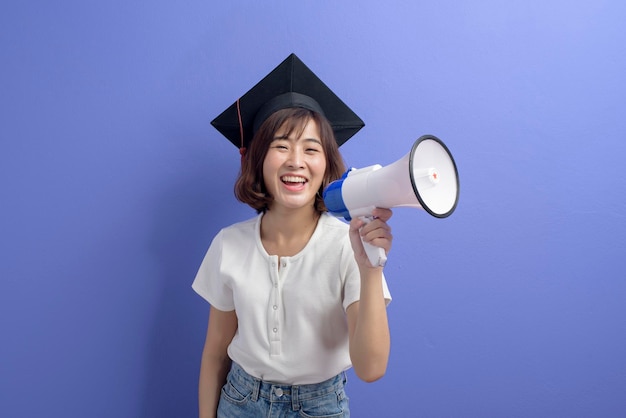 Um retrato de estudante asiático graduado segurando megafone isolado estúdio de fundo roxo