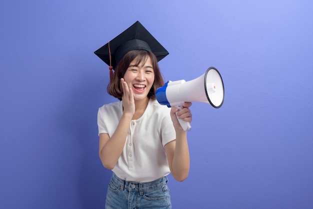 Um retrato de estudante asiático graduado segurando megafone isolado estúdio de fundo roxo