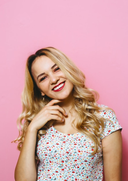 Foto um retrato de mulher loira jovem e alegre, posando de moda em uma parede rosa