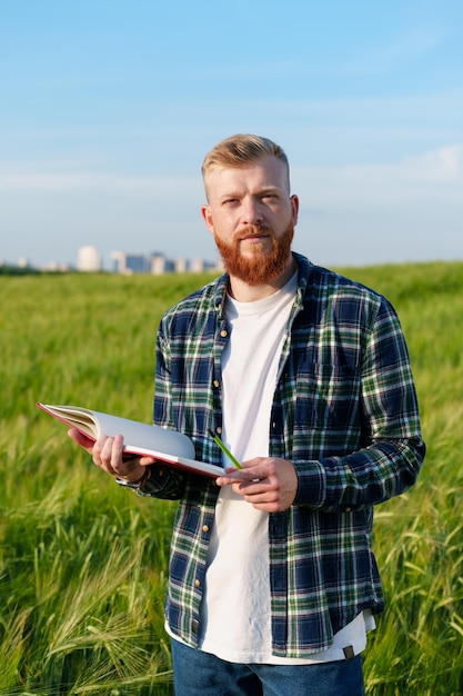 Um retrato de um agricultor com um notebook fica em um campo com trigo no contexto de uma megalópole preparação da colheita durante a crise alimentar no mundo