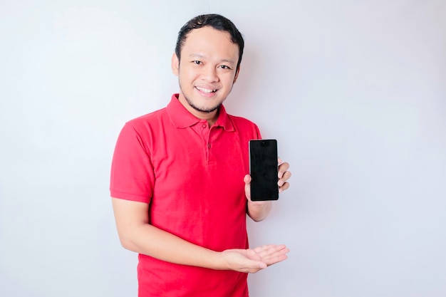 Um retrato de um homem asiático feliz está sorrindo e mostrando espaço de cópia em seu smartphone vestindo camisa vermelha isolada por um fundo branco