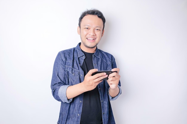 Um retrato de um homem asiático sorridente está sorrindo e segurando seu smartphone vestindo uma camisa azul marinho isolada por um fundo branco