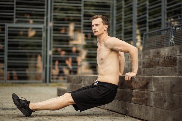 Um retrato de um homem musculoso focado em roupas de treino pretas fazendo mergulhos treinando os músculos do braço