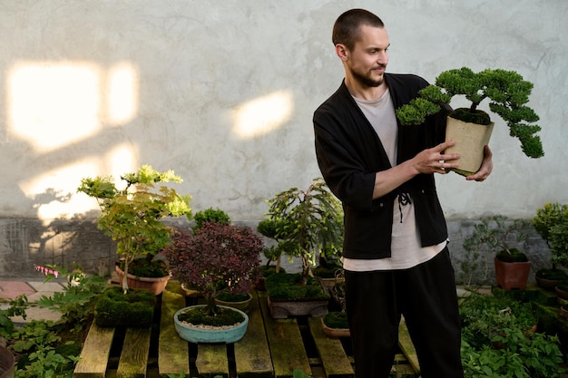 Um retrato de um jovem bonito com um bonsai nas mãos no fundo branco