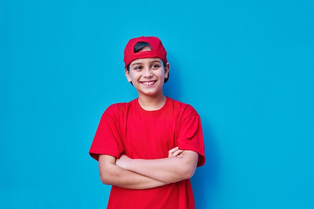 Um retrato de um menino feliz e sorridente em uma camiseta vermelha e boné com os braços cruzados