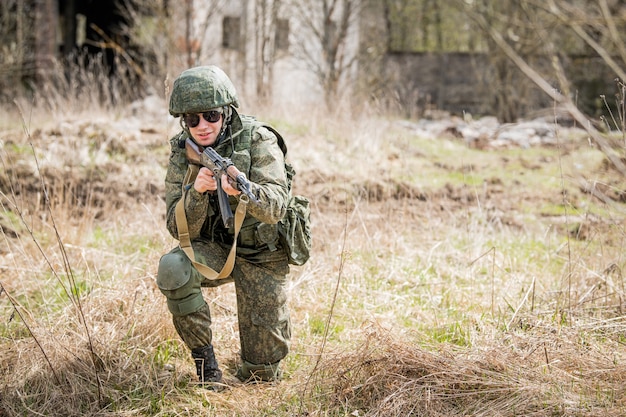 Um retrato de um soldado totalmente equipado mirando com um rifle em um campo de batalha no meio da grama seca.